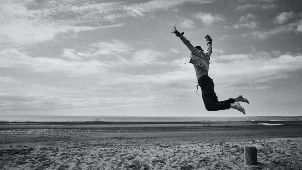 grayscale photo of man jumping on beach