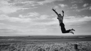 grayscale photo of man jumping on beach